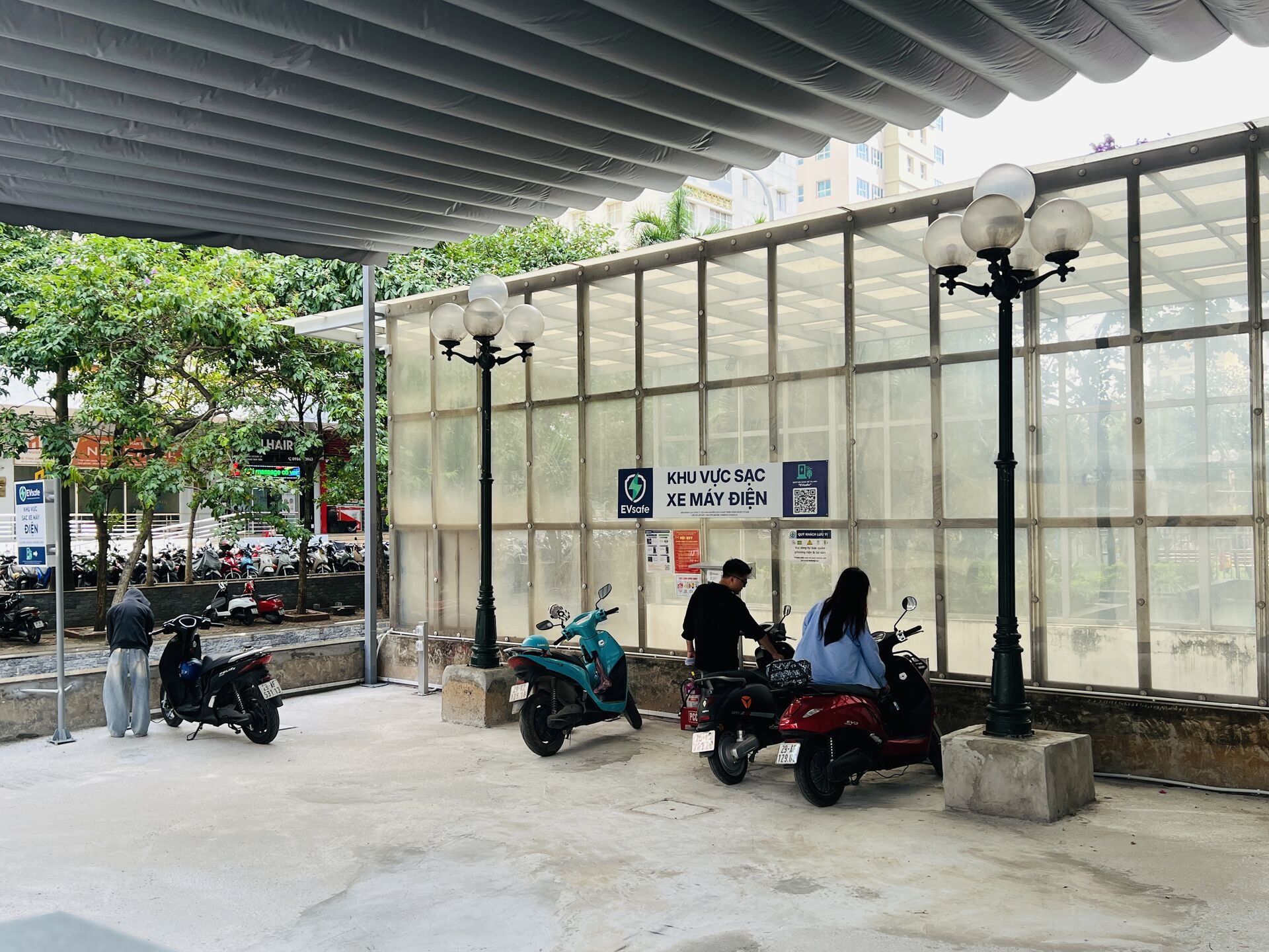 Hình ảnh trạm sạc xe máy điện trước chung cư mini ở quận Thanh Xuân với cư dân đang sạc xe điện, không gian sạch sẽ và hiện đại