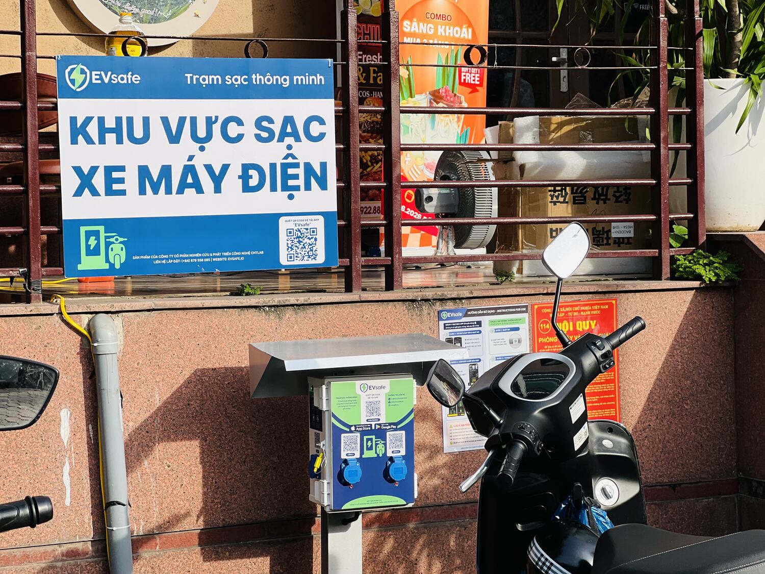 Biển khu vực sạc xe máy điện EVsafe và hộp sạc treo tường tại quán Chill Desk, quận Cầu Giấy, Hà Nội